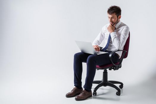 emotional young guy in office clothes working on a laptop computer and sitting on a chair