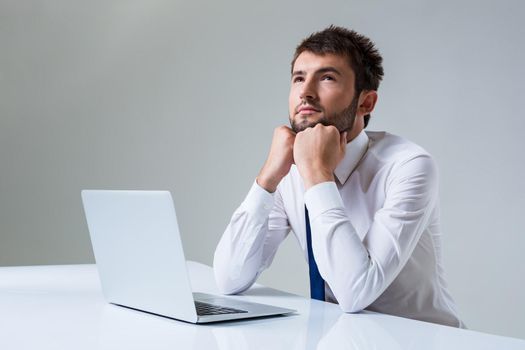 young man thinking uses a laptop computer while sitting at a table. Office clothing