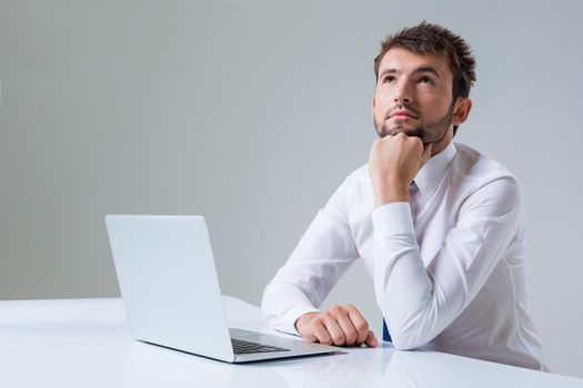 young man thinking uses a laptop computer while sitting at a table. Office clothing