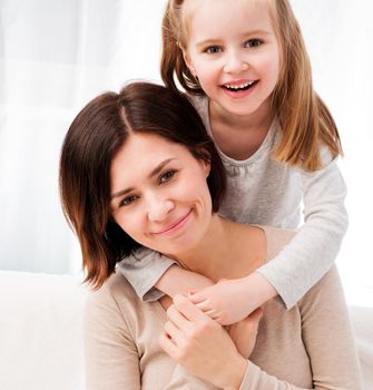 Portrait of happy mother and daughter hugging and smiling at camera in the living room