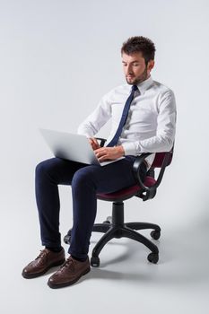 emotional young guy in office clothes working on a laptop computer and sitting on a chair