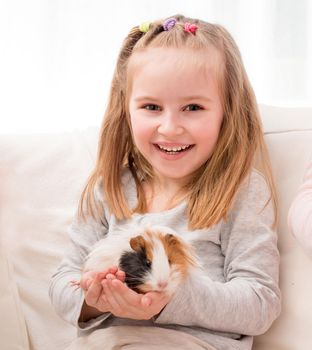 Cheerful little girl holding guinea pig on hands and smiling looking at camera