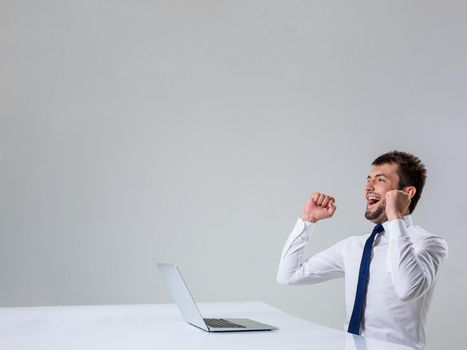 the young man behind the laptop. It uses a computer while sitting at a table. enjoys hands up. Office clothing. Copyspace