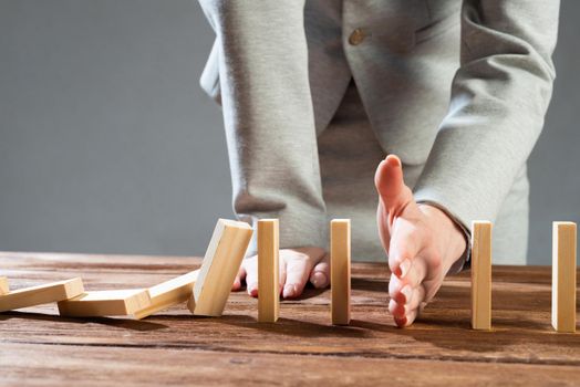 Close up female hand interrupting domino effect. Operative business solution, strategy and successful intervention. Business assistance concept with wooden blocks. Protection from economic crisis.