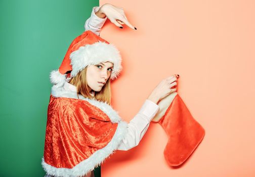 Young woman or cute serious girl with pretty face in christmas santa holds Christmas stocking on orange green isoalted background