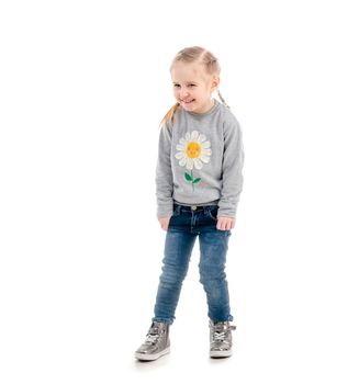 Little blonde child smiling awkwardly, wearing blue jeans and gray sweatshirt, isolated on white background