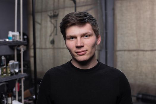 A young European guy portrait with dark hair in a black sweatshirt in a hairdresser.