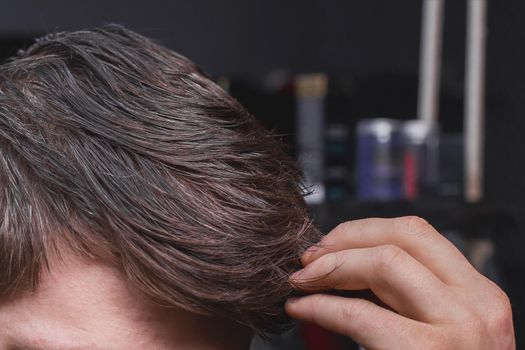 A man's hand touches his dark long hair necessary for a haircut and in need of hairdressing services.