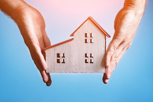 White wooden house in a male hands. White background. Housing concept