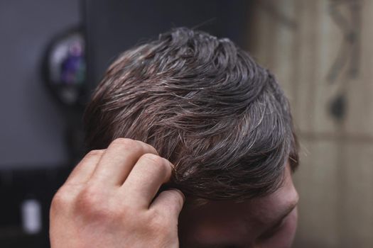 A man's hand touches his dark long hair necessary for a haircut and in need of hairdressing services.