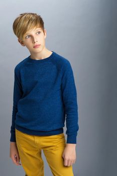 Portrait of stylish teenage boy. Handsome teenager wearing blue pullover and yellow pants posing in studio. Shot of student teenager with serious face expression