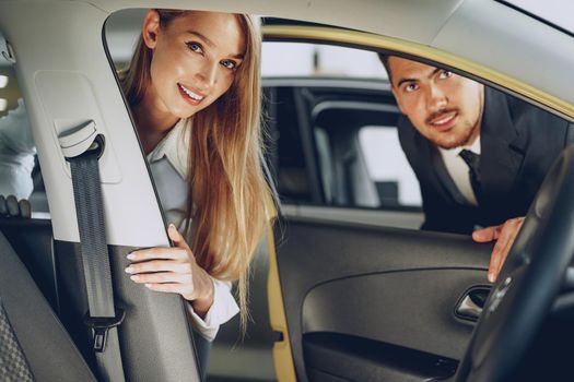 Man car dealer showing a woman buyer a new car in car salon