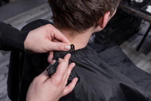 The hands of a barber or hairdresser prepare a client with dark long hair for a haircut and hairdressing services.