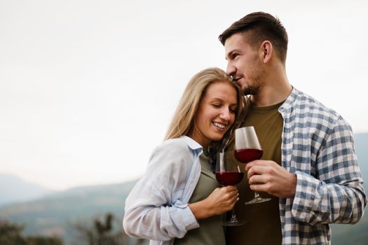 Smiling couple toasting wine glasses outdoors in mountains, close up portrait