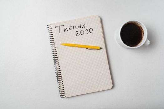 Trends 2020. Handwritten text. Notebook and Cup of coffee on white background