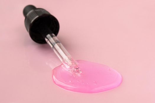 Pipette with fluid hyaluronic acid on pink background. Cosmetics and healthcare concept closeup. Dose of serum or retinol with air bubbles. Flat lay. Luxury gel or beauty product presentation in macro