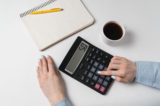 Hand of young woman using calculator. Budget planning concept. White background, top view.