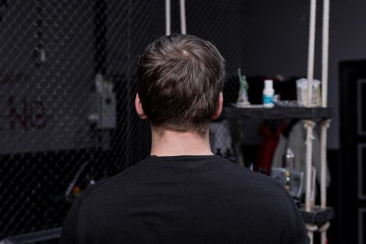 Portrait occiput of a guy of Caucasian appearance with dark hair in a black sweatshirt against the background of a hairdresser. The need for hairdressing services and cutting overgrown hair.