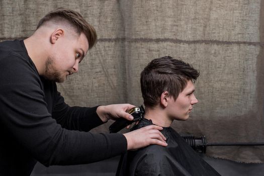 Barber or hairdresser cuts the back of the head of a guy with dark hair with a machine. Hairdressing.