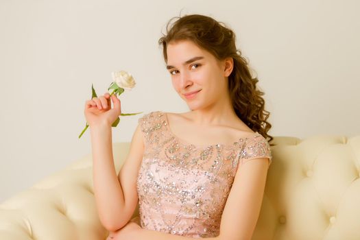 Very beautiful teen girl sitting on a couch holding a flower in her hand. The concept of style and fashion.