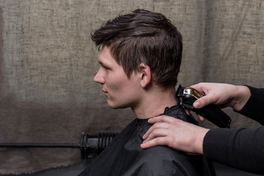 Barber or hairdresser cuts the back of the head of a guy with dark hair with a machine. Hairdressing.