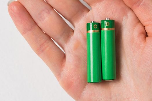 Two green AA batteries on womens palm. Generic accumulator on white background. closeup.