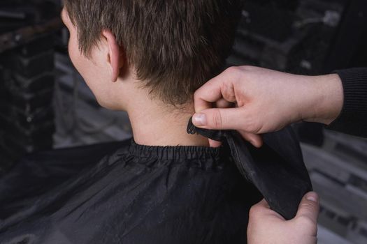 The hands of a barber or hairdresser prepare a client with dark long hair for a haircut and hairdressing services.