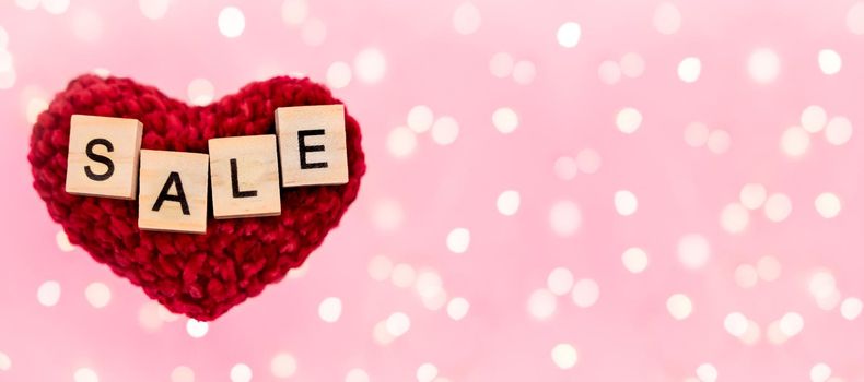Banner word sale on red plush heart blurred pink background with copy-space with beautiful bokeh from garlands lights. Concept holidays black friday, christmas, valentine's day and seasonal discounts