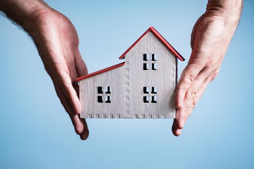 White wooden house in a male hands. White background. Housing concept