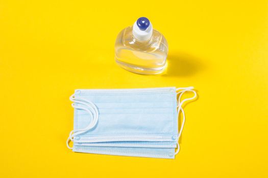 Alcohol gel hand sanitizer and disposable hygienic mask on yellow background