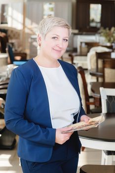 Portrait of a middle-aged business woman. The owner and director of the furniture business is standing near the table. Strong woman with a short haircut.