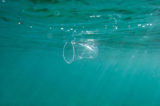 Plastic cup floats underwater in the open ocean. Environmental pollution concept.