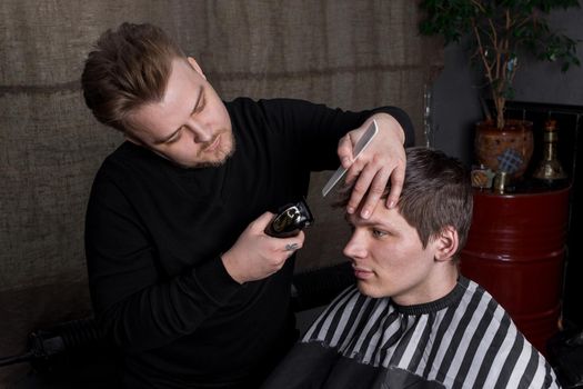 The hands of a barber or hairdresser cut a client with dark hair with an automatic machine and a comb in the barbershop. Hairdressing.