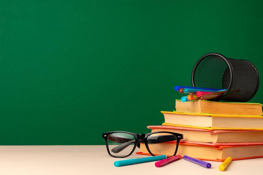 School supplies on wooden desk against green chalkboard front view
