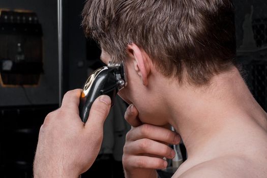 A guy with a bare torso cuts his dark hair with an electric machine. Hair care at home.