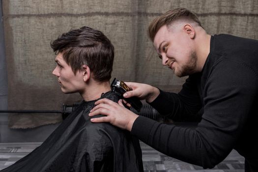 Barber or hairdresser cuts the back of the head of a guy with dark hair with a machine. Hairdressing.