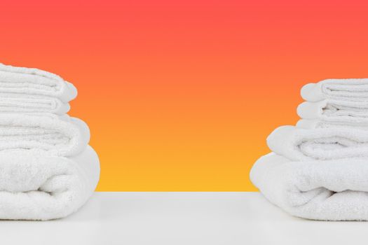 Stacked clean towels on white table against color background, front view
