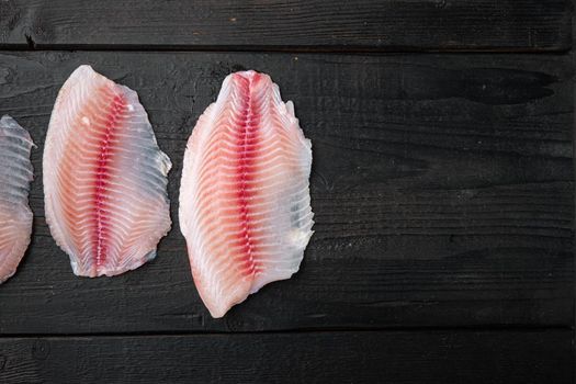 Tilapia fish, skinless meat, on black wooden table, top view with copy space for text