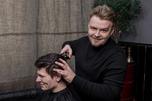 A positive barber or hairdresser of Caucasian appearance cuts the client of a guy with dark hair. Hairdressing.