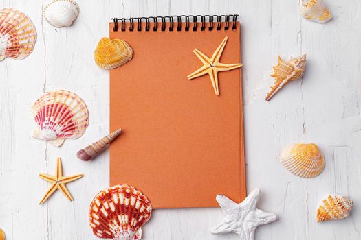 Brown open notepad surrounded by sea shells on white wooden table, copy space