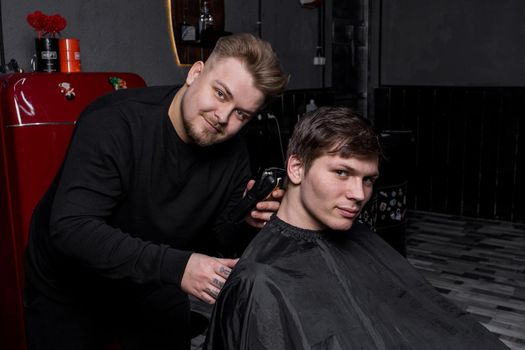 A positive hairdresser or barber of European appearance cuts a satisfied client with dark hair in a hairdresser. Hairdressing.