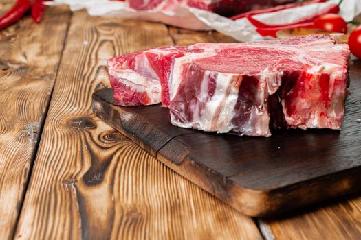 Raw T-bone steak with herbs on wooden board, close up