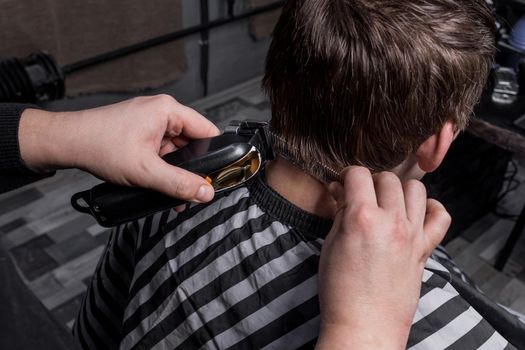 The hands of a barber or hairdresser cut the back of the client's head with dark hair with an automatic machine and comb in the barbershop. Hairdressing.