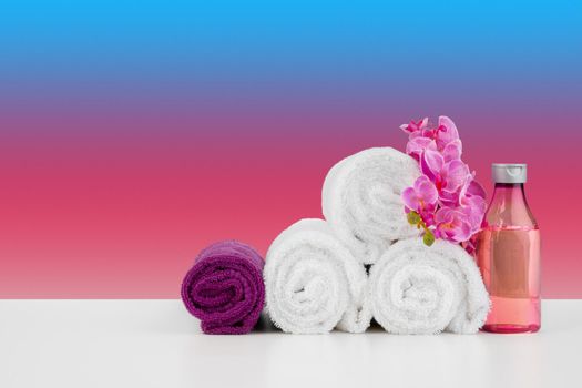 Stack of white towels and bottles of skincare on white table, front view