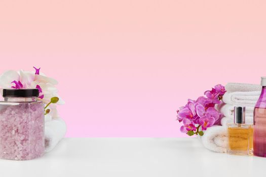 Stack of white towels and bottles of skincare on white table, front view