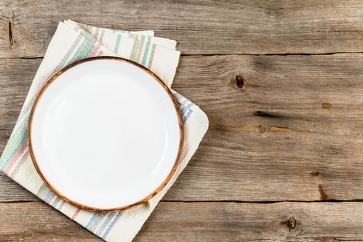 Empty white ceramic dish on rustic wooden table with cloth napkin