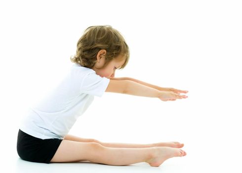 Cute little girl performs gymnastic exercises on the floor in the studio on a white background. The concept of sports, the physical development of children