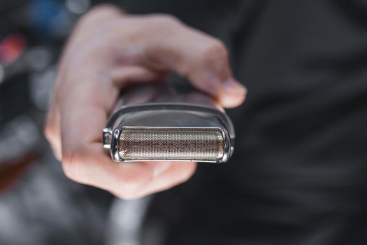 The hand of a barber or hairdresser holds an automatic clipper for cutting and shaving close-up against the background of the salon.