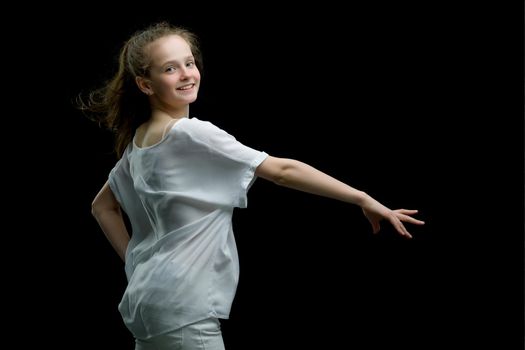 A strong wind blows on the face and clothes of a beautiful little girl of school age. Hair and clothes are fluttering in the wind, and the girl is happy about it. On a black background. Studio photo session