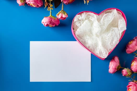 Greeting card and open gift box on a blue background. Blank greeting card and open pink heart-shaped gift box on a blue background. Place for text, design for valentines day.